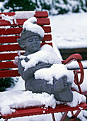 Figur 'Dozy' im Schnee auf rotem Gartenstuhl