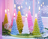 Pastellfarbene Kerzen in Tannenbaumform auf hellgrünem Tablett am Fenster