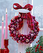 Kranz aus kleinen roten, rosa und lila Weihnachtsbaumkugeln an Fenstergriff