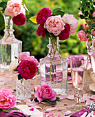 Rosa (Rosen) in Glasflaschen auf Mosaiktisch mit Blütenblättern, Glas