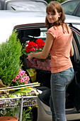 Junge Frau lädt frisch gekaufte Pflanzen ins Auto