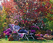Woman on wooden lounger in front of autumn bed with Amelanchier (Rock Pear)