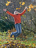 Young woman jumping and throwing leaves in the air