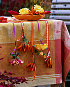 Rosa (roses), Capsicum (ornamental pepper) on ribbons at the side of the table, bowl