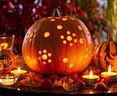 Cucurbita with punched holes as a lantern, autumn leaves