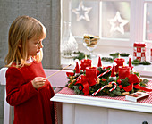 Girl lights candles on Advent wreath with Juniperus, Abies