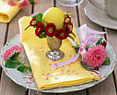 Tellerdekoration mit Blüten von Tausendschön um Osterei und auf dem Teller