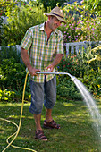 Mann gießt Rasen mit dem Schlauch und der Gießbrause