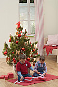 Boy sitting with presents in front of Pinus (pine tree)