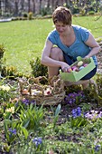 Woman filling Easter nest in flowerbed with colourful Easter eggs