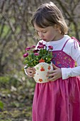 Little girl with bellis (daisy) in a planter