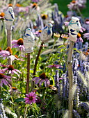 Handgetöpferte Steckfiguren zwischen Echinacea purpurea