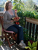 Frau genießt frisch geerntete Tomaten auf dem Balkon