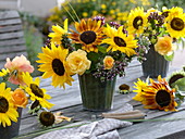 Sträuße in Blechvasen mit Sonnenblumen und Rosen auf Holztisch
