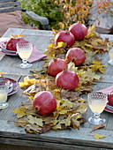 Tischdekoration mit Granatäpfeln auf einem Läufer aus Herbstlaub