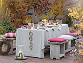 Herbstlich gedeckter Tisch mit Heide, Rosenstrauß und Chrysanthemenkränzen