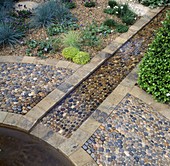 Ein mit Steinen eingefasster, mit Kieselsteinen gefüllter Bachlauf verläuft durch den Evening Standard Eros Garden