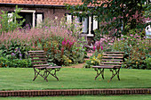 VIEW TO THE FARMHOUSE PAST TWO SEATS. INB / G IS ASTILBE Var TAQUETII 'PURPURLANZE'. DESIGN-PIET / ANJA OUDOLF