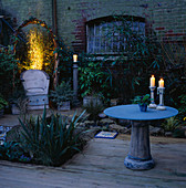 NIGHT-LIT CORNER of Garden with CERAMIC CHAIR & GLASS / CERAMIC TABLE with CANDLES. Designer: Emma LUSH. Water Feature by Mark LAURENCE