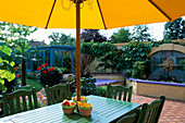 Green TABLE AND CHAIRS with Yellow CUSHIONS On TERRACOTTA Patio with Water Feature BEHIND. THE NICHOLS Garden, READING
