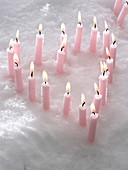 Brennende rosafarbene Kerzen im Schnee, in Herzform aufgestellt