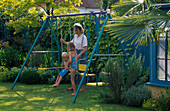 HAZEL, Robert AND JANE PLAYING On THE SWING with Blue FENCE AND Golden HOP, NICHOLS Garden, READING