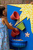 Spielen in der Eimer-Wasserkaskade, blaues Brett mit gelbem Mosaik, bunte Terrakotta-Töpfe, Muscheln, Seesterne und fließendes Wasser