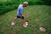 Dinosaurier-Fußabdrücke. Junge, der über die in den Rasen gehauenen Zementformen von Dinosaurier-Fußabdrücken springt