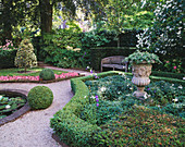 Privatgarten mit Buchsbaumhecke, geschnittenen Stechpalmen, Beetbegonien, Steinurne und Holzbank