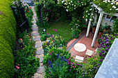Seitengarten mit Rose 'Goldfinch' über der Terrasse, Rose 'Open Arms' am Tor, Aconitum, Clematis 'Warsaw Nike', 'Betty Corning' und 'Etoile Violette'