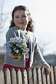 Girl behind fence with bouquet of Myosotis (Forget-me-not)