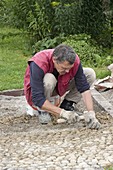 Mann legt Pflaster aus Kieselsteinen (Mittelkorn - Größe) in Riesel-Zement