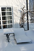 Verschneite Liege und kleiner Tisch auf Terrasse im Winter