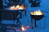 Winterliche Terrasse mit Feuerkorb und Windlichtern auf dem Tisch