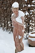 Verschneite Terrakotta-Frau vor Hecke aus Carpinus