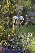 Figur 'Gartenkönig' auf Pfahl im Herbstbeet mit Aster (Herbstastern)