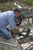 Mann legt Abrundung der Beeteinfassung aus Granit-Steinen