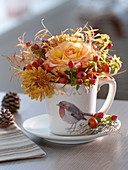 Cup with robin decoration filled with roses and rosehips