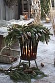 Kranz aus Picea omorica (Fichte) mit Zapfen auf Feuerkorb mit Kerzen