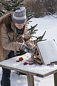 Woman filling bird house with sunflower seeds, apples (Malus)