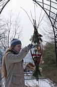 Frau füllt selbstgebaute Futterstation aus Zweigen von Cornus