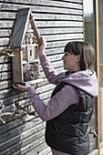 Frau hängt Insektenhotel an Hauswand