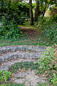 Noun: kleine Naturstein-Treppe führt in den Schattengarten unter großen Bäumen