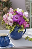 Bouquet of Gladiolus (gladioli) and Humulus (hops) in blue jug