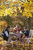 Family at table in golden autumn leaves under maple tree