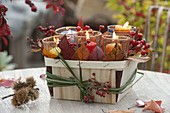 Small chip basket filled with candle jars, autumn leaves and pinks