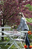 White sitting area under Malus 'Scarlet' with red flowers