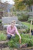Frau erntet Karotten im Biogarten