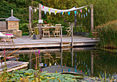 Schwimmteich mit Nymphaea (Seerosen) und Schilf, Sitzgruppe auf Holzdeck unterm Sonnensegel