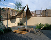 Dachterrasse aus Holz mit Gräsern, Agapanthus, Sonnensegeln, Liege, Tisch und Klappsesseln, fest eingebaute Bank an der Wand entlang